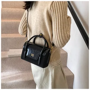 Detail of a black glossy mini crossbody bag with a gold metal logo on a beige sweater