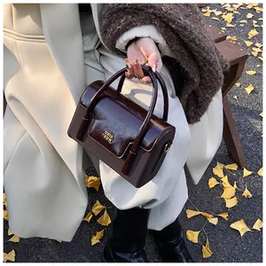 Detail of structured crossbody bag with brown glossy flap and gold logo in autumn setting
