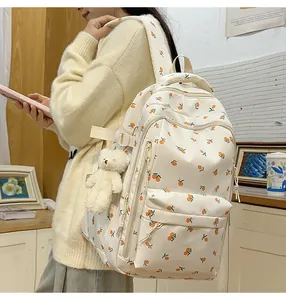 Detail view of a cream casual backpack with orange prints and a white plush bear charm