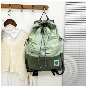 Detail of light green drawstring backpack with zip pocket and woven ropes on white wall