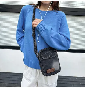 Detail of washed black denim crossbody bag with adjustable strap and logo patch