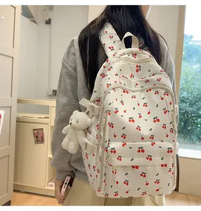 Detailed back view of a white cherry print backpack with a cute plush bear charm accessory