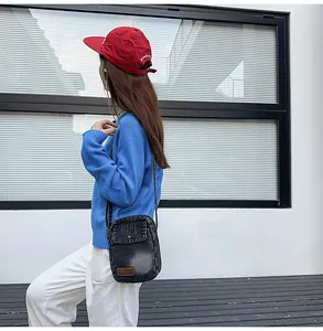 Detail of dark denim crossbody bag with flip buckle and leather label on outdoor model