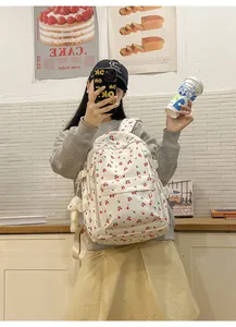 Detail of off-white backpack with red cherry print and a cute plush bear pendant