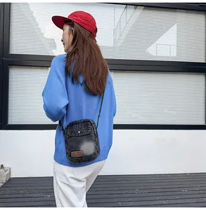 Outdoor lifestyle shot of a black washed denim crossbody bag with metal buckle detail