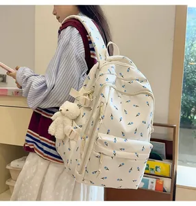 Detail of cream backpack with blue floral pattern and cute white bear keychain accessory
