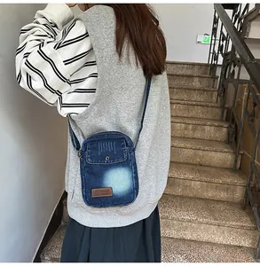 Close-up of a blue denim crossbody bag with a leather logo patch on a female model