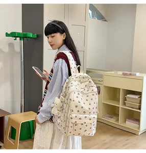 Detailed view of white canvas backpack with pink strawberry prints and bear charm