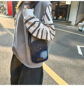 Detail of vintage blue denim crossbody bag with Street leather patch and metal studs