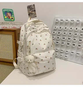Detail of white floral backpack with pink patterns, side buckles and a bear plush pendant