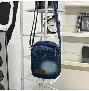 Detail of blue denim crossbody bag featuring a vintage leather label and metal buckle