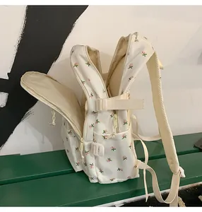 Side view of cream backpack with floral embroidery and adjustable straps on a green bench