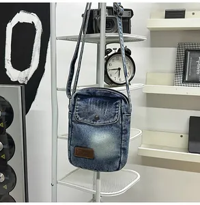 Detail of blue washed denim crossbody bag with vintage leather logo on white rack