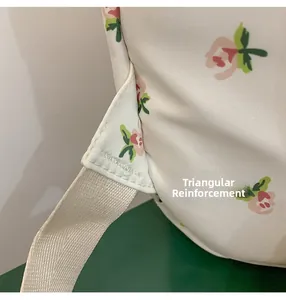 Detail showing the reinforced triangular stitching on white floral canvas backpack straps