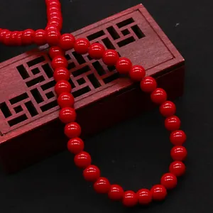 Vibrant red polished stone round beads shown on a traditional hollow wooden jewelry box