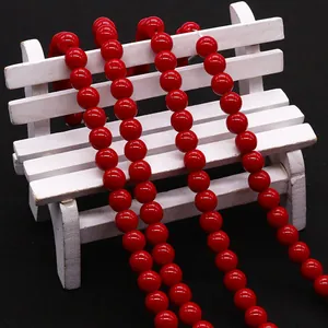 Polished red round beads for DIY jewelry making displayed on a small white bench