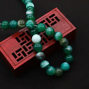 Perle tonde in agata verde striata su una scatola di legno rossa con sfondo nero