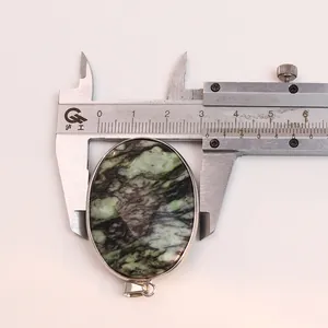 Macro view of oval natural stone pendant being measured by a metal caliper