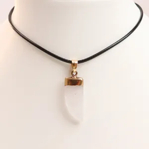 Macro detail of horn shaped white crystal stone pendant with golden metal clasp and black rope