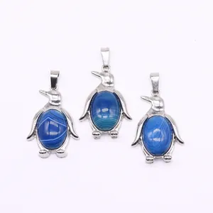 Drie zilveren pinguïnhangers met ovale blauw gestreepte stenen op witte achtergrond