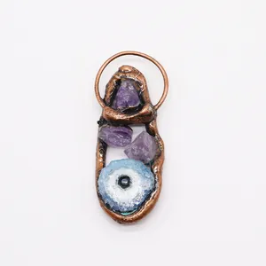 Detail of copper wrapped pendant featuring purple amethysts and a blue agate evil eye stone