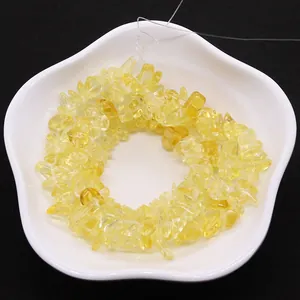 Irregular yellow citrine stone beads on string in white petal dish over black background