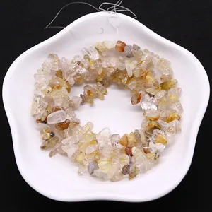 Brins de perles en quartz rutilé doré naturel sur un plat blanc pour la création de bijoux