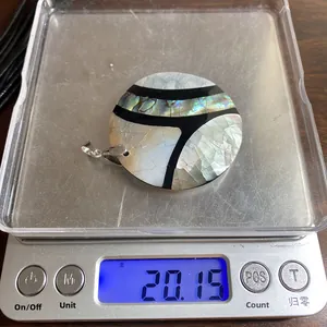 Foto macro de un colgante redondo de nácar con incrustación de abulón que pesa 20,15g en báscula