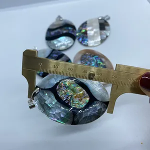 Dettaglio di vari ciondoli in conchiglia di abalone misurati con un calibro di ottone