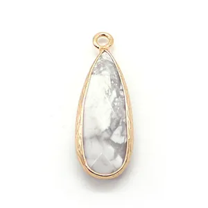 Macro view of teardrop white turquoise pendant with textured gold plated metal edges