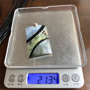 Bilancia digitale che mostra un peso di 21,34 g per un ciondolo rettangolare in abalone