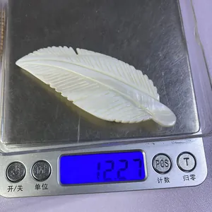 Détail d'un pendentif en nacre sculpté en plume de cygne pesant 12,27 g sur une balance