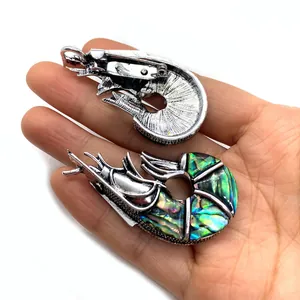 Garnaalvormige hanger en broche met abalone inleg op de hand met witte achtergrond