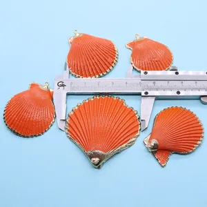 Gros plan de cinq pendentifs coquillages orange mesurés avec un pied à coulisse