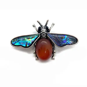Macro shot of bee brooch featuring red agate abdomen and iridescent abalone shell wings