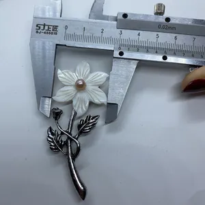 Macro shot showing measurement of a carved shell flower brooch with pink pearl and silver stem