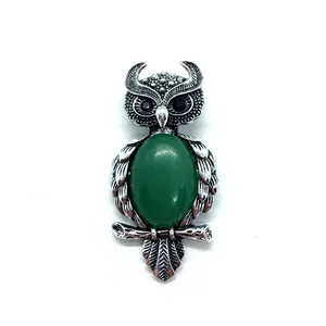 Macro detail of owl-shaped brooch with green stone inlay and fine feather texture