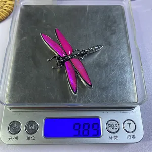 Macro detail of a dragonfly brooch made of pink enamel and silver metal on a digital scale