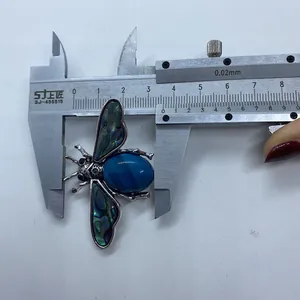 Detail view of a bee brooch featuring abalone shell wings and blue striped agate stone