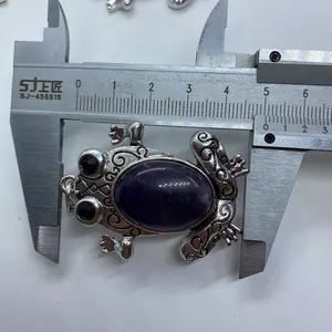Detailed measurement of a frog pendant with purple stone using a metal caliper