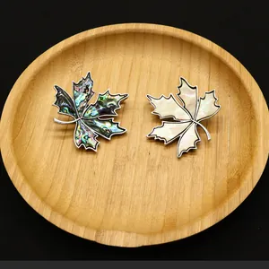Broches en nacre en forme de feuille d'érable sur plateau bois et fond noir