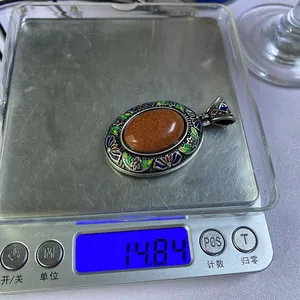 Dettaglio macro di un ciondolo cloisonné ovale vintage che pesa 14,84g su una bilancia