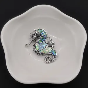Zinc alloy seahorse brooch with iridescent abalone shell inlay on a white floral plate