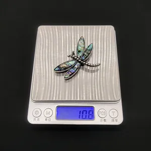 Dettaglio spilla a libellula da 10,8g con ali in conchiglia iridescente su una bilancia