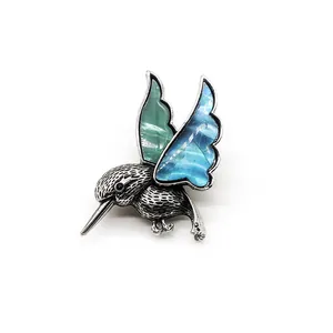Détail d'une broche colibri avec ailes en nacre irisée et texture de plumes argentées