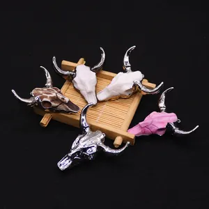 Five assorted resin bull skull pendants with metallic horns on a bamboo mat background