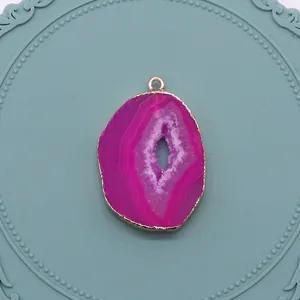 Vue détaillée du pendentif géode d'agate rose rouge avec bords dorés sur plateau bleu