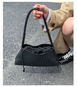 Dettaglio della trama in pelle nera intrecciata di una borsa sottobraccio con coulisse