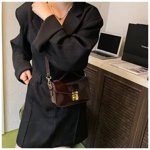 Close-up of a glossy dark brown patent leather shoulder bag with a gold metal buckle