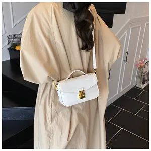Back view of a white patent leather crossbody bag with gold hardware on a model